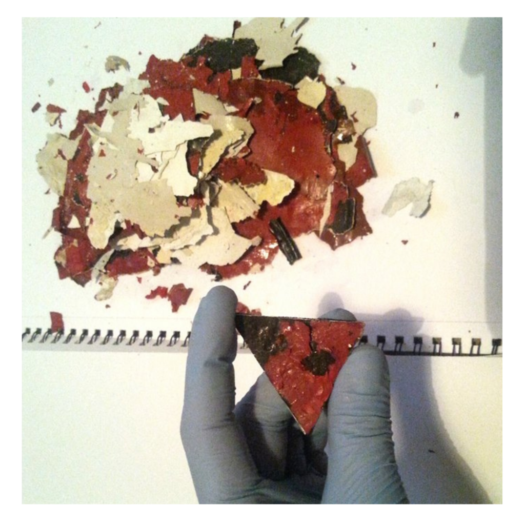 A gloved hand holding paint and plaster on a triangular support